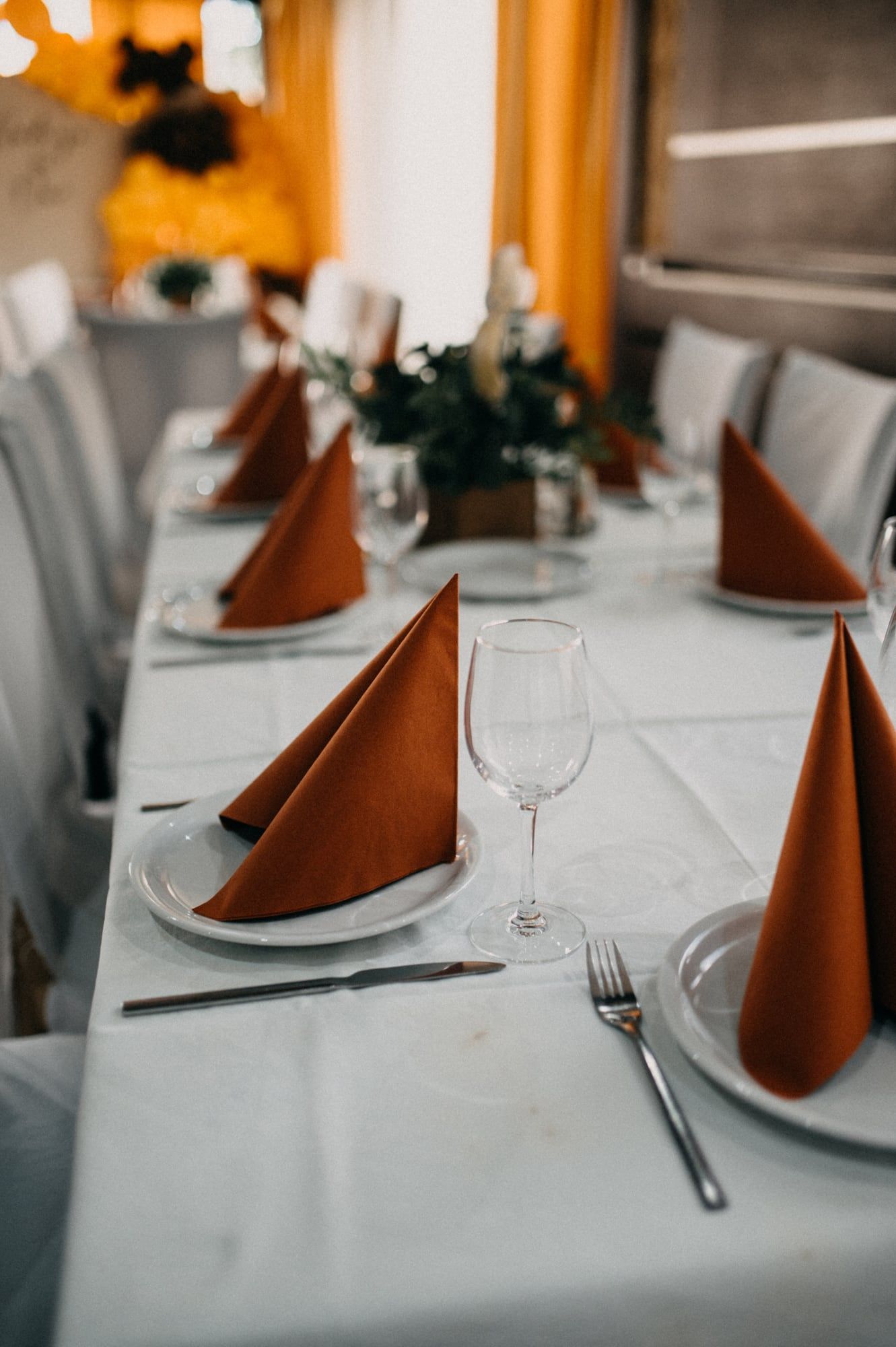 A long formal dinner table in white linen, with folded copper napkins at each place.