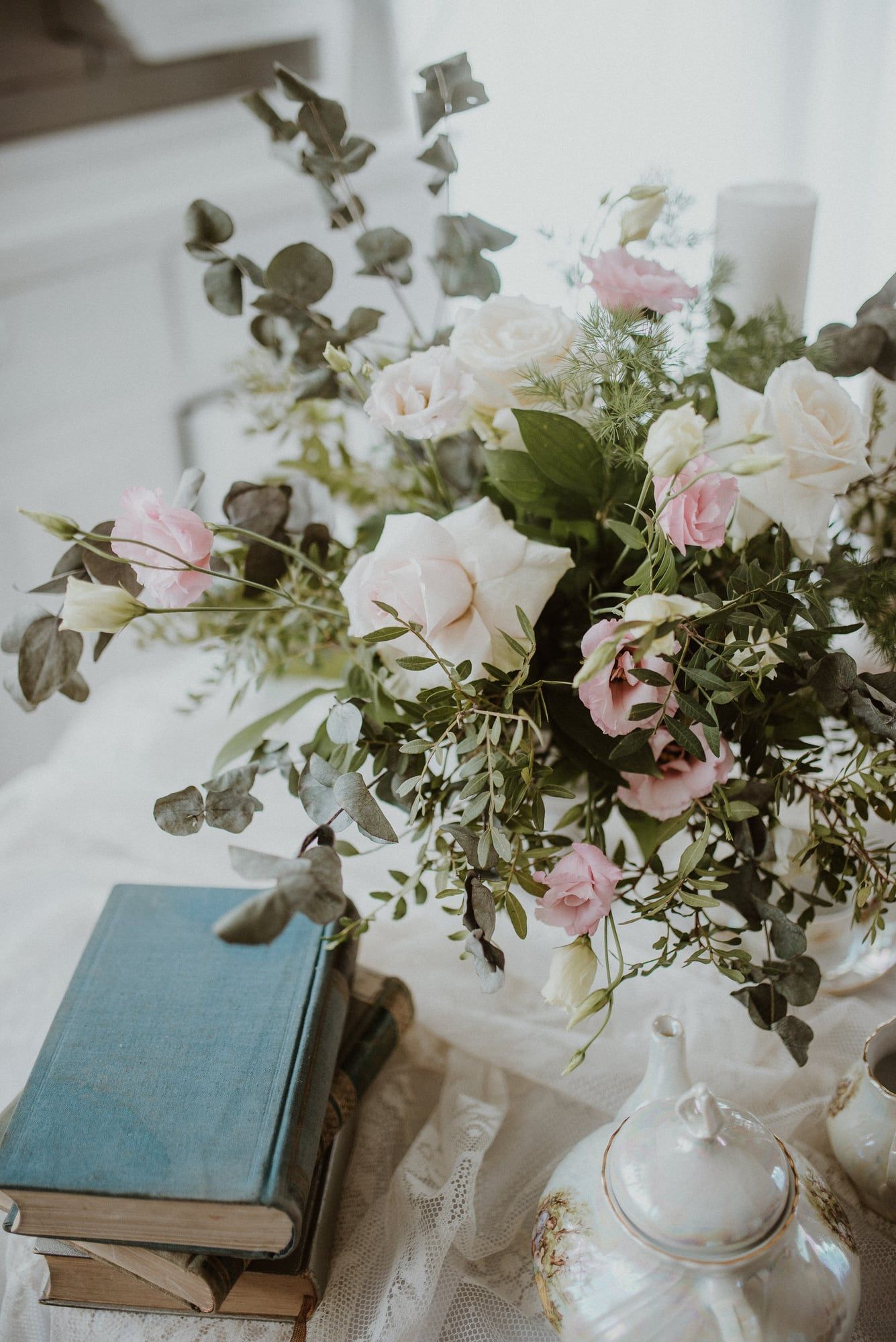 A loose arrangement of pale pink and white roses beside a small stack of old books.