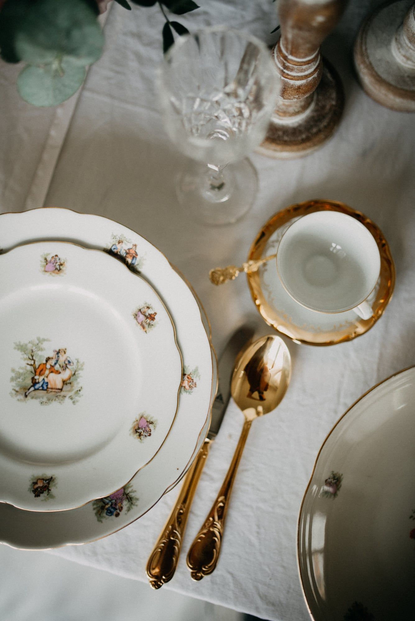 Floral-patterned china, a gilt-rimmed cup, and gold cutlery on white linen, seen from above.